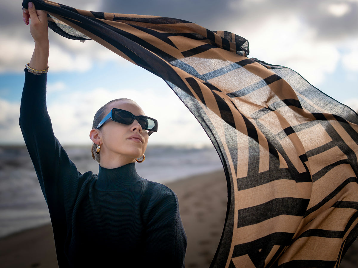 Woman lifting a printed scarf in the wind on a beach